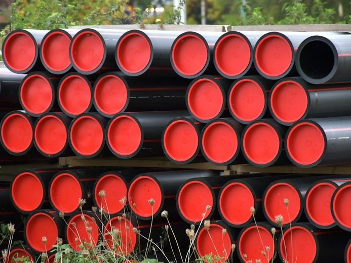 Large-diameter HDPE pressure pipes stacked in a yard, red transit end caps covering each bore.